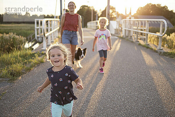 Verspieltes Mädchen mit Familie und Hund bei Sonnenuntergang unterwegs