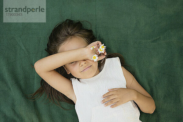 Mädchen hält Kamillenblüten auf einer Decke