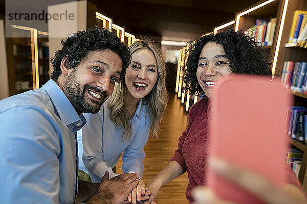 Glückliche Kollegen  die in der Bibliothek ein Selfie mit dem Smartphone machen