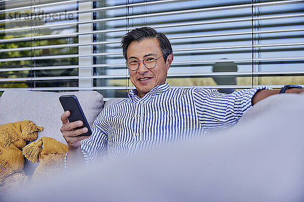 Smiling mature man with smart phone sitting on sofa