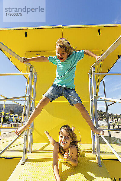Glückliche Geschwister spielen zusammen auf der gelben Rettungsschwimmerhütte