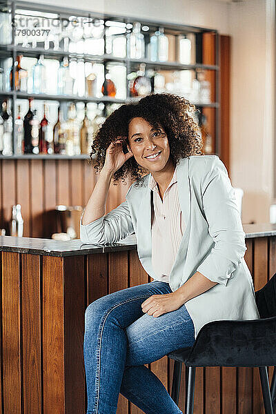 Lächelnde Frau sitzt auf einem Stuhl in der Bar