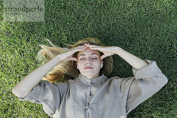Frau mit geschlossenen Augen reibt sich den Kopf  indem sie im Gras liegt