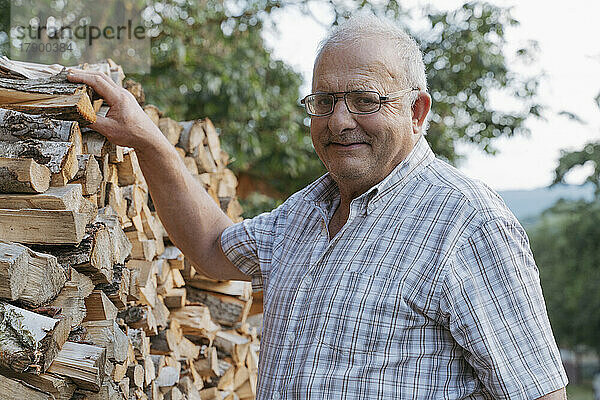 Lächelnder älterer Mann neben einem Stapel Brennholz