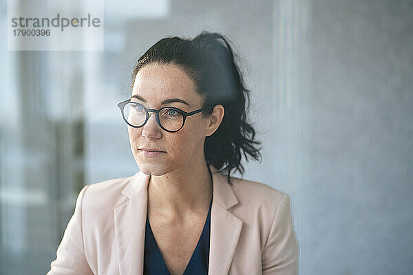 Nachdenkliche Geschäftsfrau mit Brille vor der Wand  durch Glas gesehen