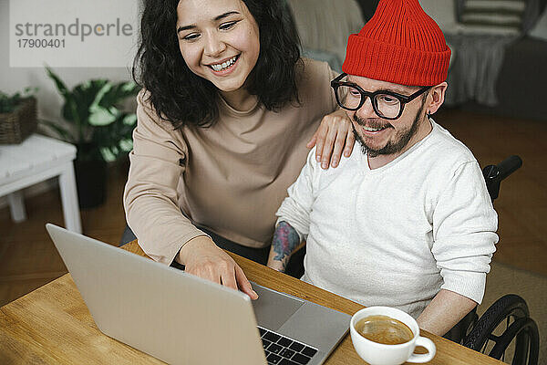 Fröhliche Frau sitzt mit ihrem behinderten Freund zu Hause am Laptop