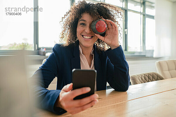 Lächelnde Geschäftsfrau mit Summerknopf  der das Auge im Büro verdeckt