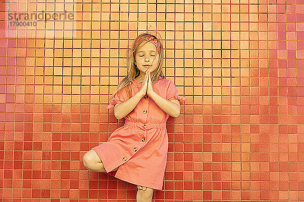 Cute girl with hands clasped in front of wall