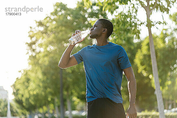 Junger Mann trinkt Wasser an einem sonnigen Tag