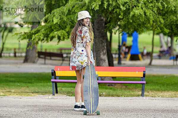 Glückliche junge Frau mit Skateboard steht im Park