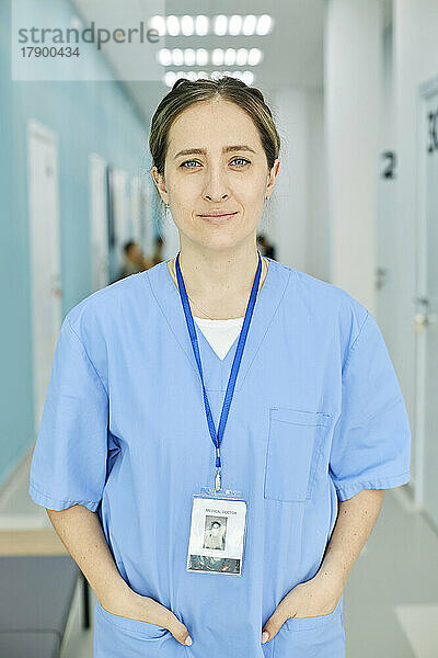 Lächelnde Krankenschwester mit den Händen in den Taschen auf dem Krankenhausflur