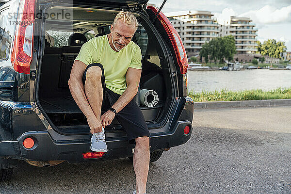 Mann sitzt im Kofferraum eines Autos und bindet Schnürsenkel