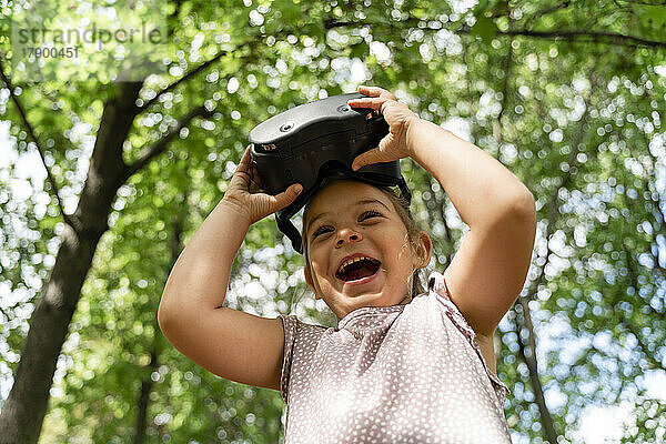 Happy girl with VR glasses standing in front of trees at park
