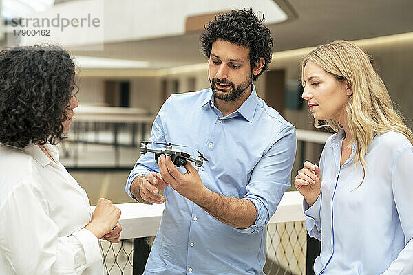 Businessman discussing over drone with colleagues in corridor