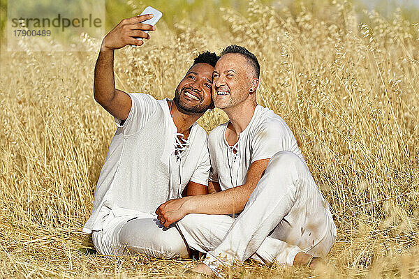 Lächelndes schwules Paar macht Selfie mit dem Smartphone im Feld