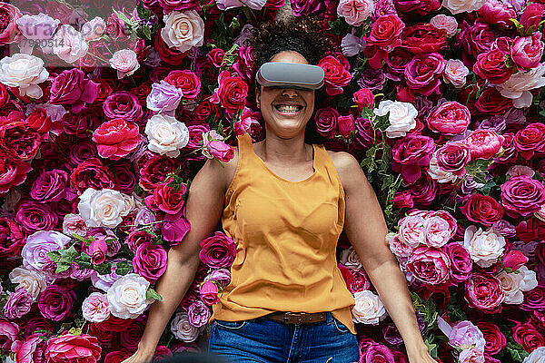 Fröhliche Frau mit VR-Brille liegt auf Blumen