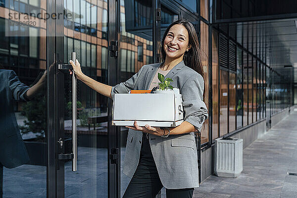Glückliche Geschäftsfrau mit einer Kiste  die neben einer Glastür steht