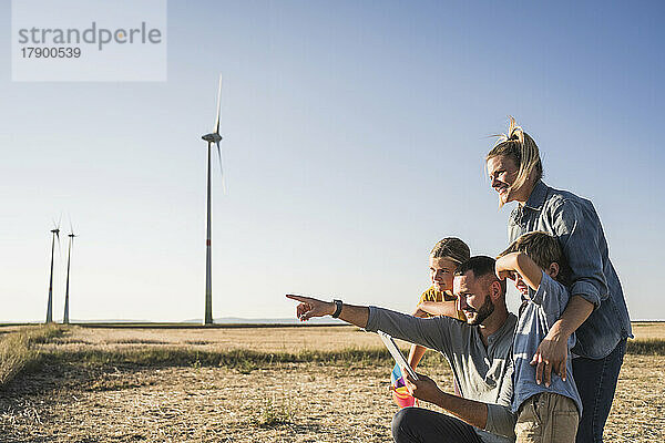 Familie nutzt digitales Tablet im Windpark und zeigt auf Windkraftanlagen