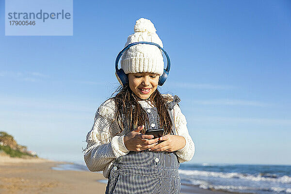 Fröhliches Mädchen  das am Strand Musik mit kabellosen Kopfhörern hört