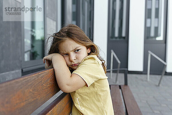 Trauriges Mädchen sitzt auf Bank vor Gebäude