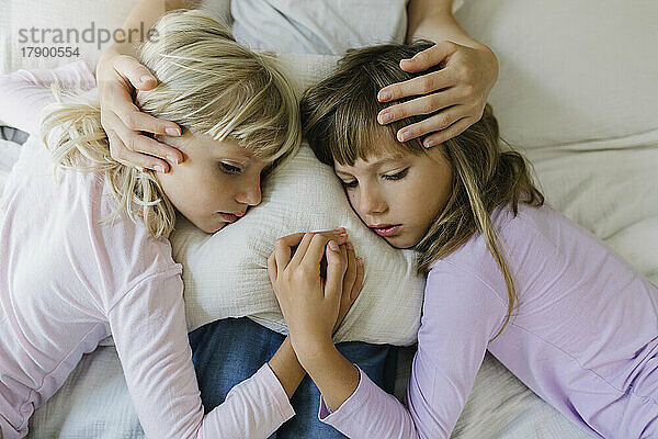 Sad siblings resting over cushion on lap of mother at home
