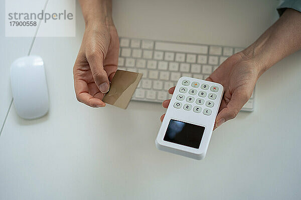 Hände einer Geschäftsfrau mit Kreditkarte und Lesegerät am Schreibtisch im Büro