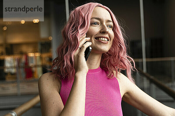 Lächelnde junge Frau mit rosa Haaren  die auf dem Smartphone spricht