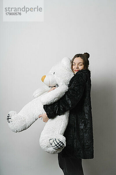 Lächelnde junge Frau umarmt Teddybär im Studio