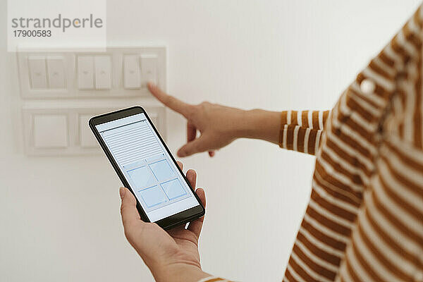 Frau berührt Schalter für Jalousien  während sie die Handy-App überprüft
