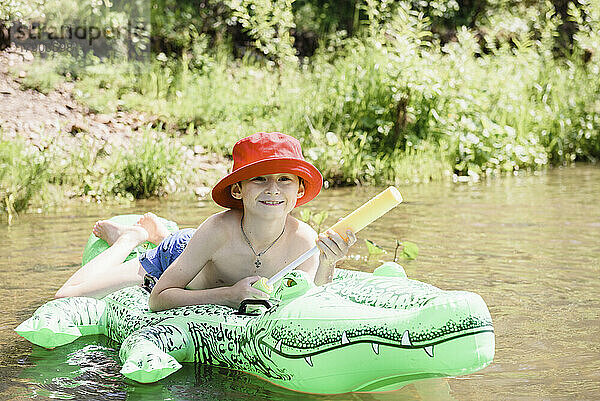 Junge mit Wasserpistole liegt auf aufblasbarem Krokodil im Fluss