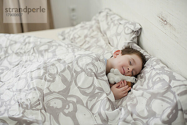 Lächelnder Junge mit Spielzeug  der auf dem Bett schläft