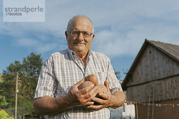 Lächelnder Bauer hält an einem sonnigen Tag Kartoffeln im Hinterhof