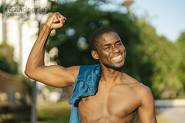 Glücklicher junger Mann  der an einem sonnigen Tag seine Muskeln spielen lässt