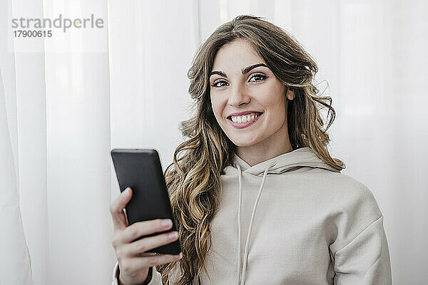 Lächelnde junge Frau mit Mobiltelefon zu Hause