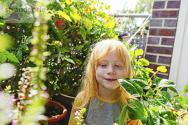 Lächelndes Mädchen  das inmitten einer Pflanze auf dem Balkon steht