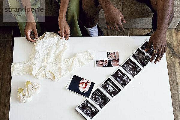 Paar mit Babykleidung und Ultraschallbildern auf dem Tisch