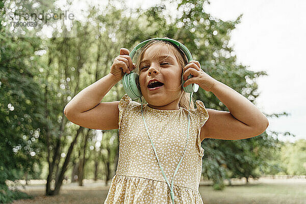 Glückliches Mädchen  das im Park Musik über Kopfhörer hört