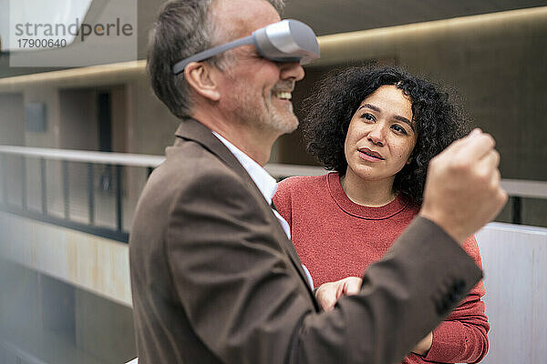 Geschäftsfrau blickt auf glückliche Kollegin mit VR-Brille im Flur