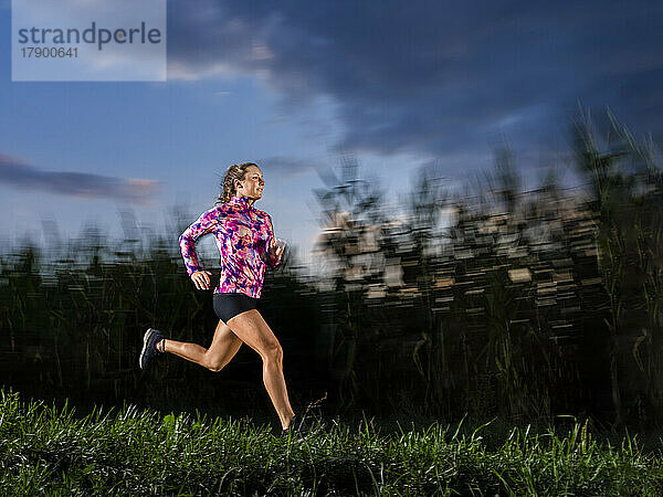 Young sportswoman running on grass at dusk