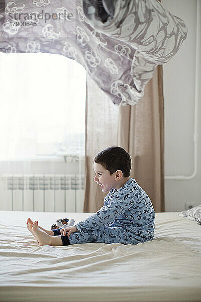 Playful boy sitting on bed under blanket in mid-air