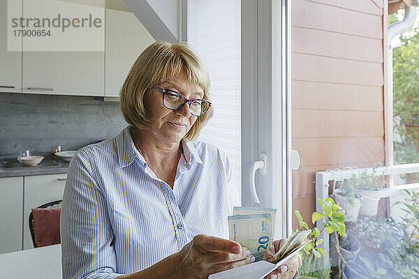 Ältere Frau mit Brille zählt zu Hause Banknoten