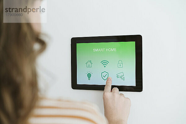Nahaufnahme einer Frau  die ein digitales Tablet mit Smart-Home-App an der Wand nutzt