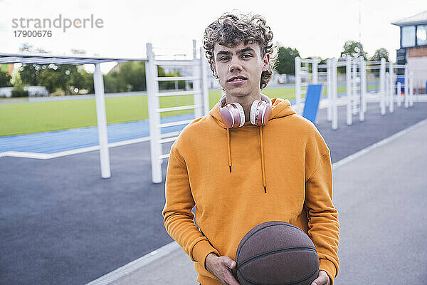 Junger Mann hält Basketball am Sportplatz