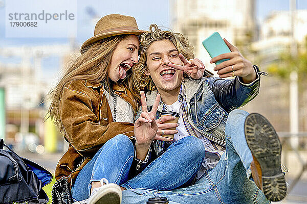 Frau streckt die Zunge heraus und macht ein Selfie mit einer Freundin  die im Urlaub ein Friedenszeichen zeigt