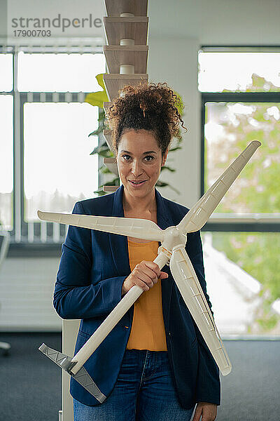 Selbstbewusste Geschäftsfrau mit Windturbinenmodell am Arbeitsplatz
