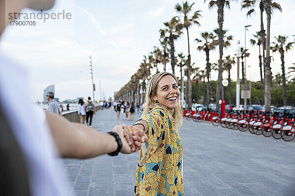 Junger Mann hält die Hand seiner glücklichen Freundin und genießt die Promenade