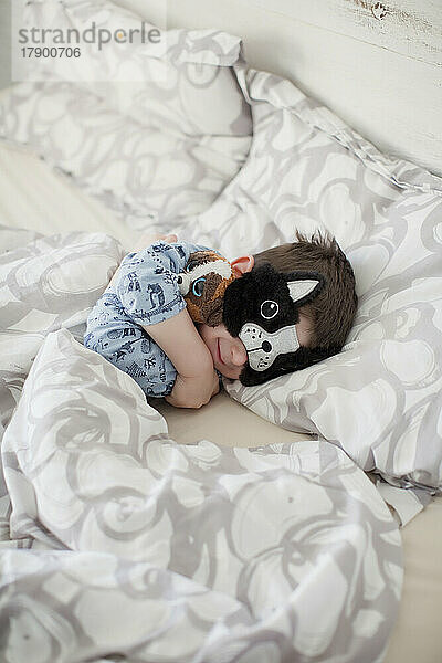 Lächelnder Junge mit Schlafmaske auf dem Bett