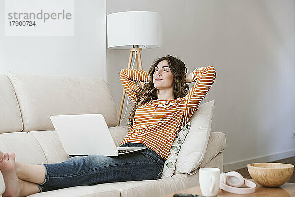 Junge Frau mit Laptop entspannt sich zu Hause auf dem Sofa