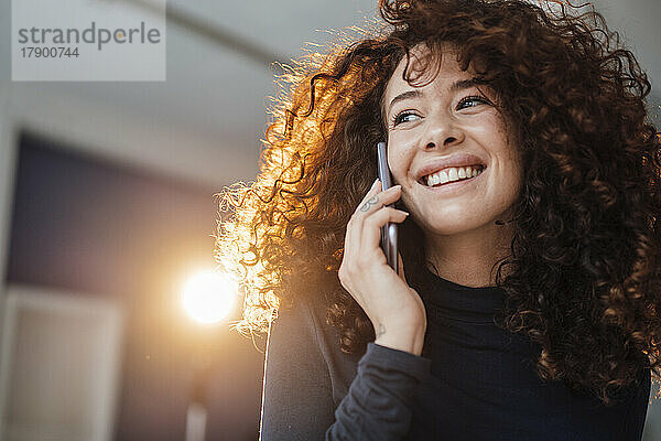 Glückliche Frau mit lockigem Haar  die mit dem Handy spricht