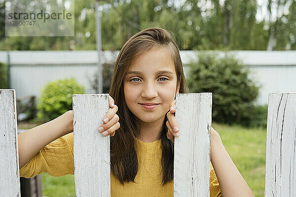 Smiling girl standing behind fence at back yard